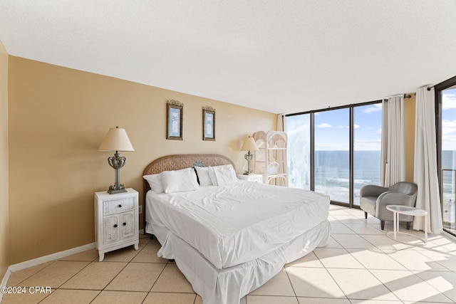 tiled bedroom featuring a water view, a textured ceiling, expansive windows, and access to exterior