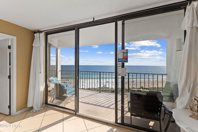 doorway to outside with light tile flooring, a textured ceiling, a view of the beach, and a water view