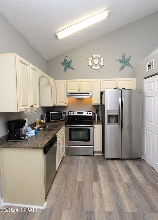 kitchen with appliances with stainless steel finishes, a textured ceiling, high vaulted ceiling, light hardwood / wood-style flooring, and sink