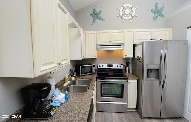 kitchen featuring dark stone counters, vaulted ceiling, light hardwood / wood-style flooring, sink, and stainless steel appliances