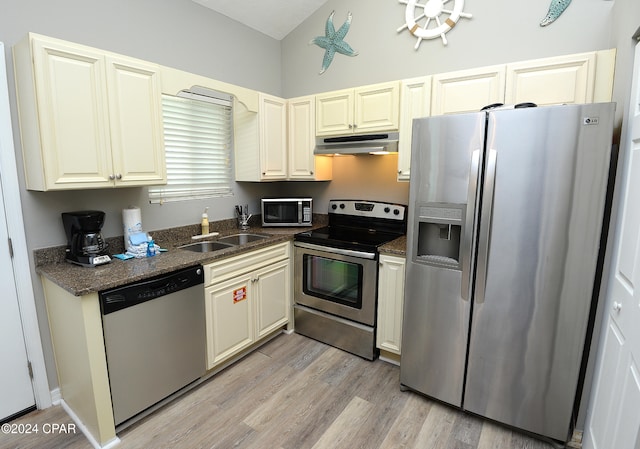 kitchen with dark stone countertops, appliances with stainless steel finishes, sink, and light wood-type flooring