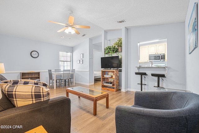 living room with vaulted ceiling, light hardwood / wood-style floors, ceiling fan, and a textured ceiling