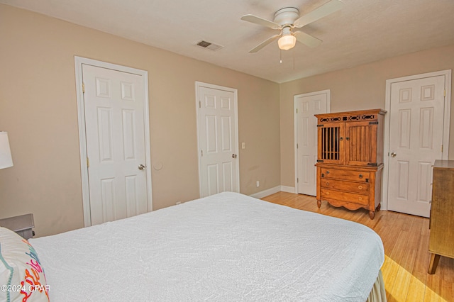 bedroom with light hardwood / wood-style floors, ceiling fan, and multiple closets