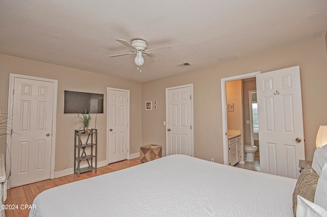 bedroom featuring ensuite bath, light hardwood / wood-style flooring, ceiling fan, and two closets