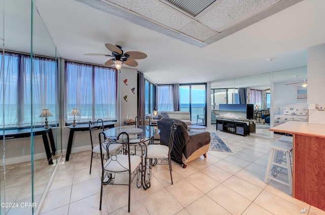 dining room featuring floor to ceiling windows, ceiling fan, light tile floors, and a water view