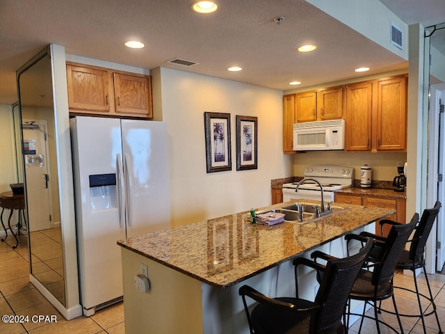 kitchen featuring light stone countertops, a breakfast bar area, white appliances, light tile flooring, and a center island