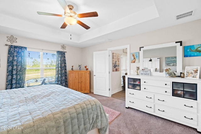 carpeted bedroom featuring ceiling fan and a tray ceiling