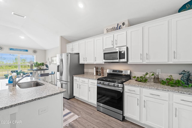 kitchen with appliances with stainless steel finishes, sink, light wood-type flooring, white cabinetry, and vaulted ceiling