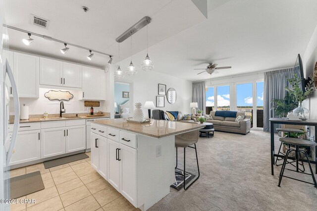 kitchen featuring a kitchen island, hanging light fixtures, ceiling fan, white cabinets, and light colored carpet