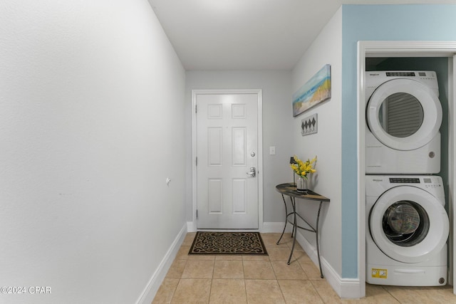 washroom featuring stacked washing maching and dryer, baseboards, light tile patterned floors, and laundry area