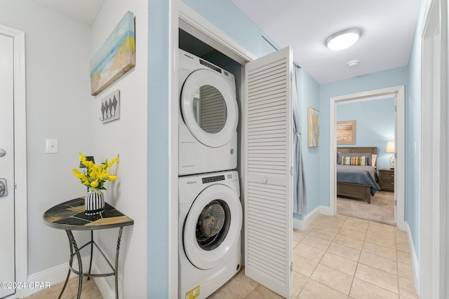 clothes washing area featuring stacked washer / dryer, laundry area, baseboards, and light tile patterned floors