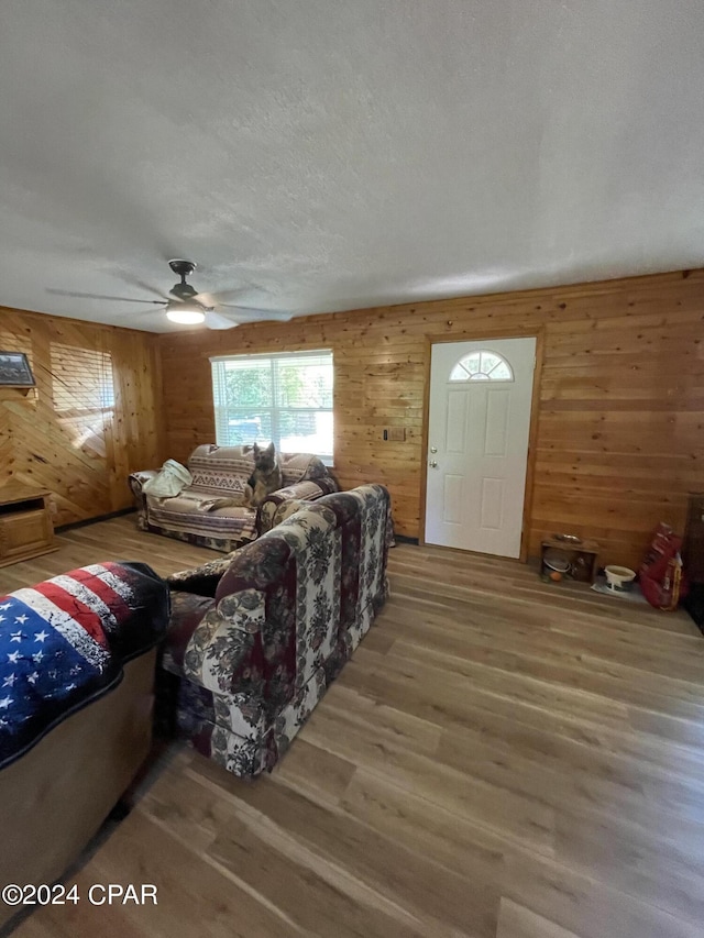 living room with hardwood / wood-style floors, a textured ceiling, wooden walls, and ceiling fan