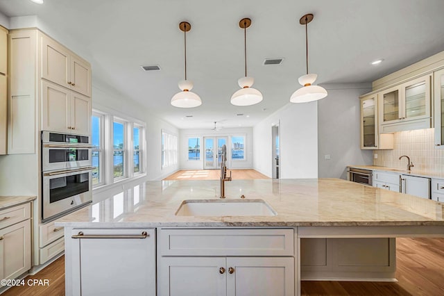 kitchen featuring stainless steel double oven, a kitchen island with sink, sink, light stone counters, and light hardwood / wood-style floors