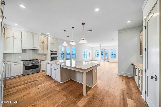 kitchen with appliances with stainless steel finishes, sink, hanging light fixtures, light hardwood / wood-style flooring, and a center island with sink