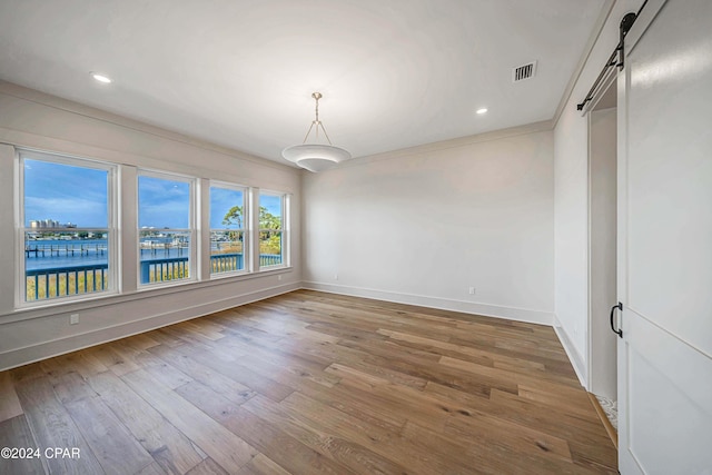 empty room featuring a water view, crown molding, hardwood / wood-style flooring, and a barn door