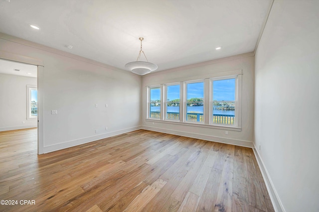 empty room featuring plenty of natural light, ornamental molding, a water view, and light wood-type flooring