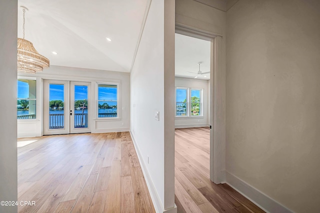 hallway featuring french doors, light hardwood / wood-style floors, lofted ceiling, and a chandelier