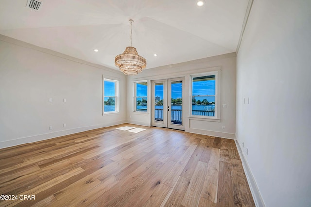 empty room featuring a chandelier, lofted ceiling, french doors, and light hardwood / wood-style floors