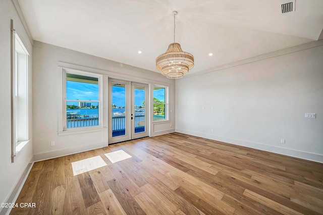 empty room with a chandelier, french doors, and light hardwood / wood-style floors