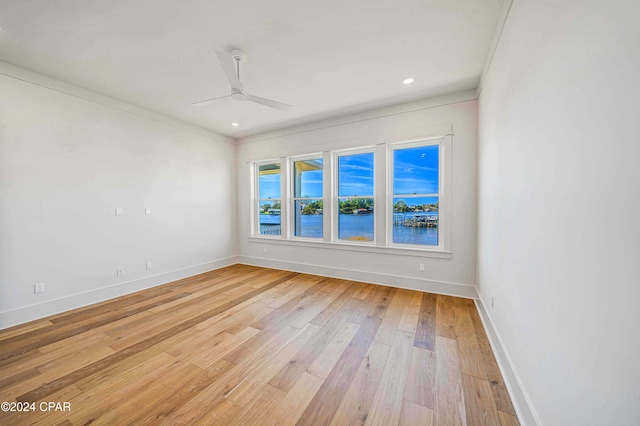 unfurnished room with light hardwood / wood-style flooring, ceiling fan, a water view, and crown molding