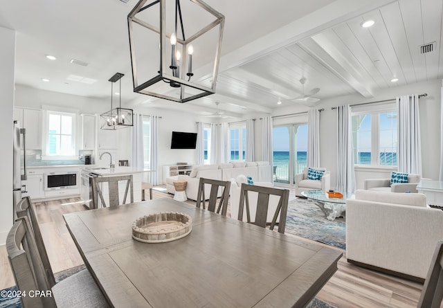 dining room with a water view, sink, beam ceiling, a chandelier, and light hardwood / wood-style flooring