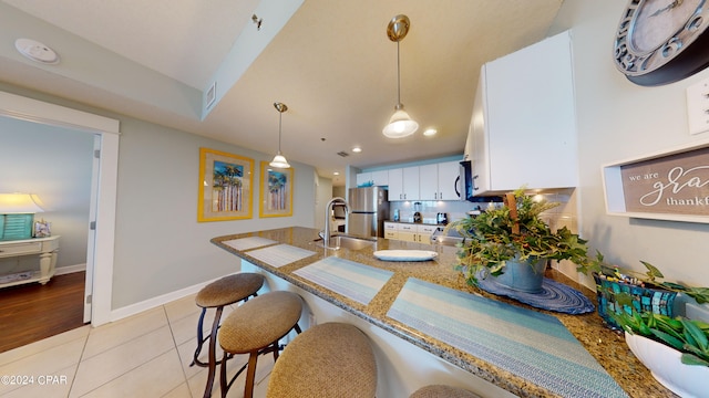 kitchen featuring white cabinets, appliances with stainless steel finishes, a peninsula, a sink, and light tile patterned flooring