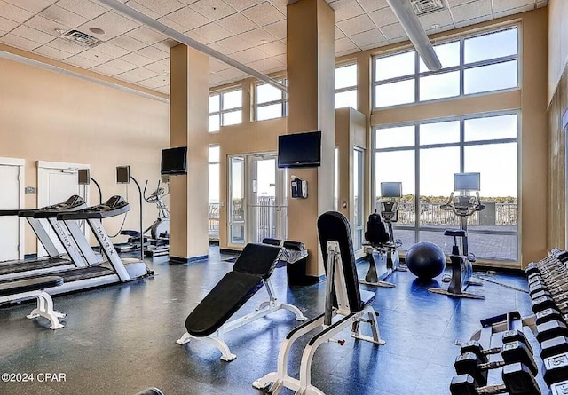 gym with visible vents, a high ceiling, a drop ceiling, and a wealth of natural light