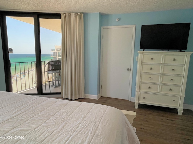 bedroom with a water view, access to exterior, light hardwood / wood-style flooring, and a textured ceiling