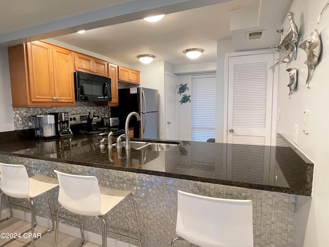 kitchen with decorative backsplash, kitchen peninsula, dark stone counters, appliances with stainless steel finishes, and a kitchen bar