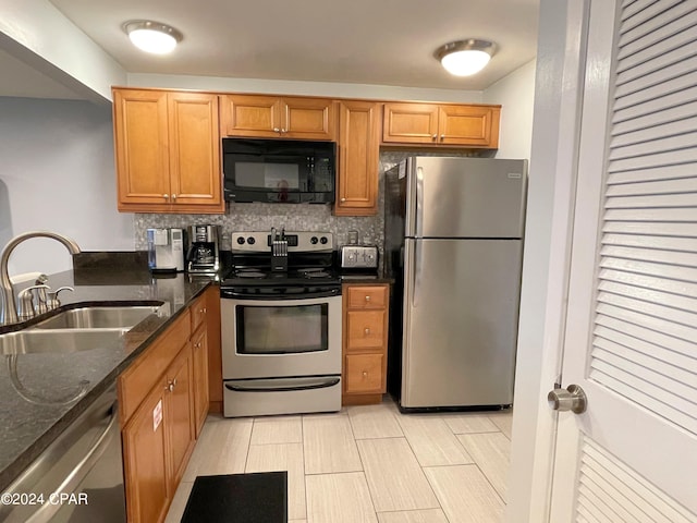 kitchen with stainless steel appliances, dark stone counters, backsplash, and sink