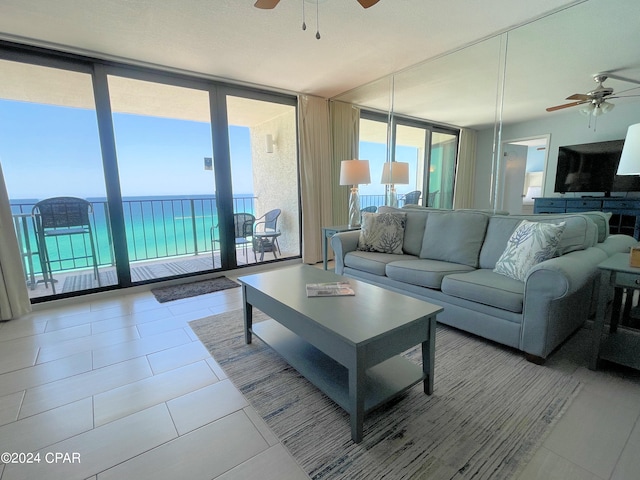 living room with light tile patterned flooring, a water view, ceiling fan, and expansive windows