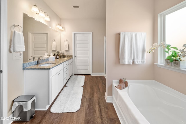 bathroom with hardwood / wood-style floors, double sink vanity, and a bathing tub