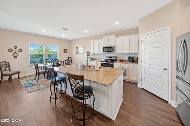 kitchen featuring dark wood-type flooring, appliances with stainless steel finishes, white cabinetry, and a kitchen island with sink