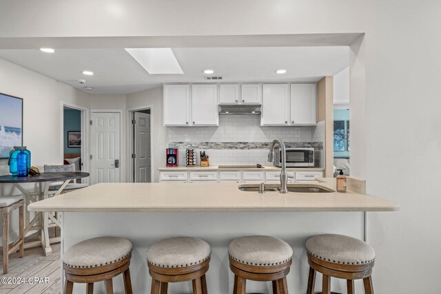 kitchen featuring kitchen peninsula, tasteful backsplash, white cabinetry, and a breakfast bar area