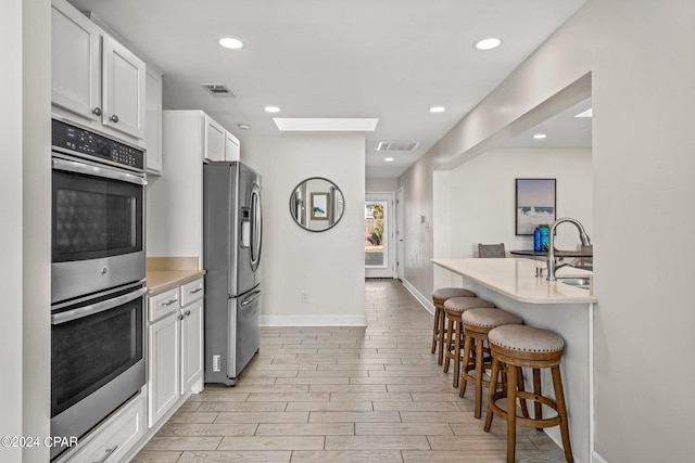 kitchen featuring appliances with stainless steel finishes, a kitchen breakfast bar, a skylight, sink, and white cabinetry