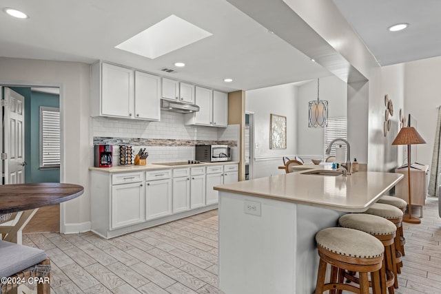 kitchen with a skylight, white cabinetry, sink, decorative backsplash, and a center island with sink