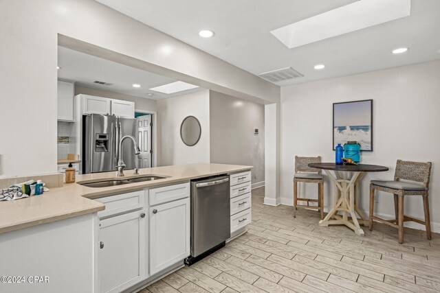 kitchen featuring sink, a skylight, decorative backsplash, white cabinetry, and stainless steel appliances