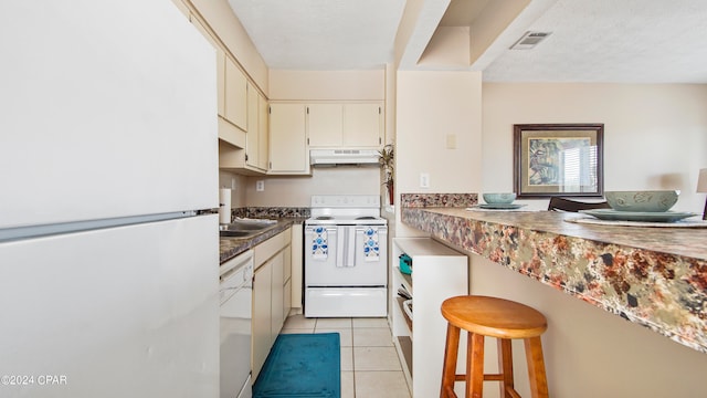 kitchen with a kitchen bar, white appliances, a textured ceiling, sink, and light tile floors