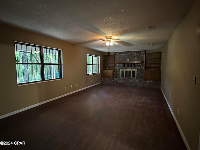 unfurnished living room featuring a healthy amount of sunlight, a textured ceiling, dark hardwood / wood-style flooring, and a brick fireplace