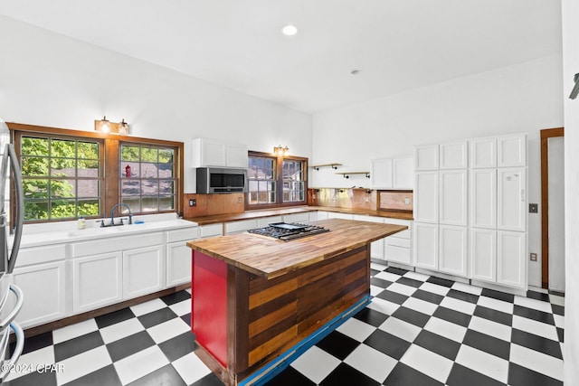 kitchen with appliances with stainless steel finishes, a kitchen island, butcher block countertops, white cabinets, and dark tile flooring