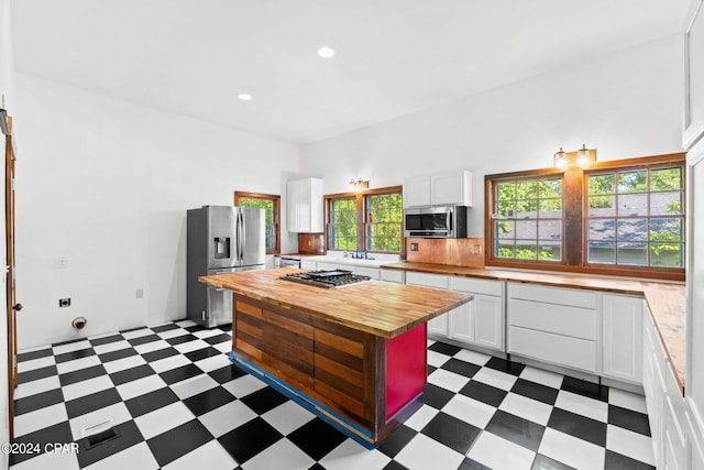 kitchen with butcher block countertops, appliances with stainless steel finishes, dark tile floors, and white cabinets