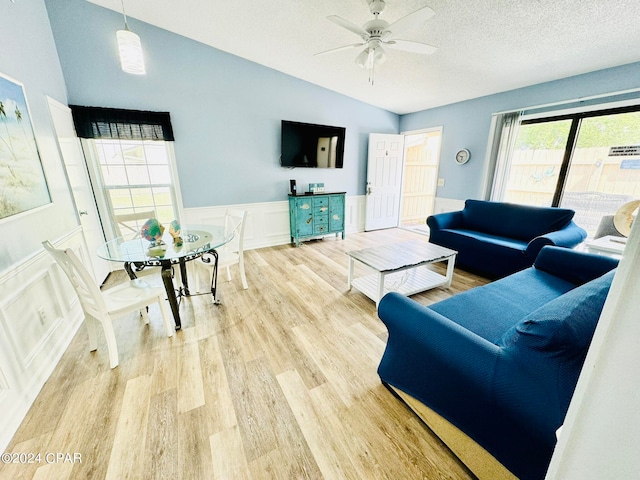 living room featuring lofted ceiling, ceiling fan, light wood-type flooring, and a textured ceiling