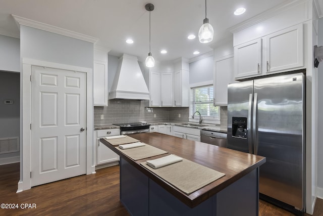 kitchen featuring premium range hood, white cabinetry, decorative light fixtures, a kitchen island, and stainless steel appliances