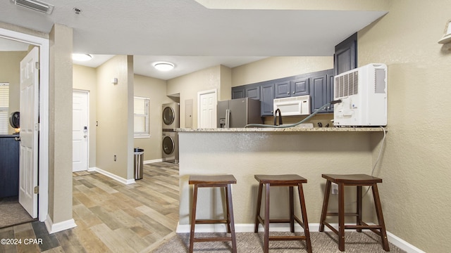 kitchen featuring stainless steel refrigerator with ice dispenser, a breakfast bar area, kitchen peninsula, and stacked washing maching and dryer