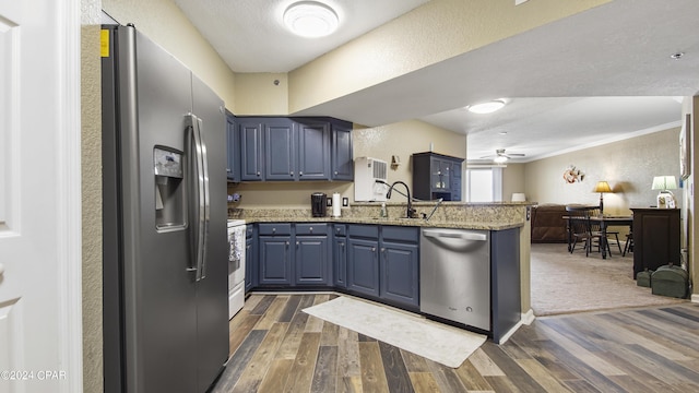 kitchen featuring appliances with stainless steel finishes, sink, blue cabinetry, dark wood-type flooring, and light stone countertops