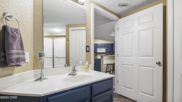 bathroom featuring hardwood / wood-style floors, a textured ceiling, a shower with shower door, and vanity