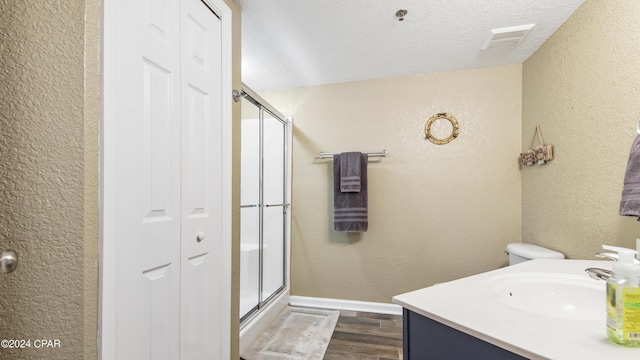 bathroom featuring hardwood / wood-style flooring, a shower with shower door, toilet, a textured ceiling, and vanity