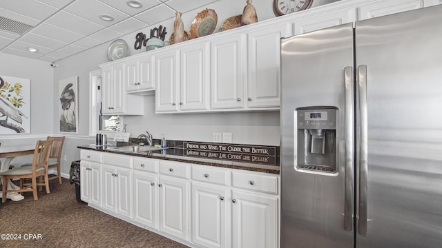 kitchen featuring stainless steel fridge with ice dispenser, sink, dark carpet, white cabinets, and a drop ceiling