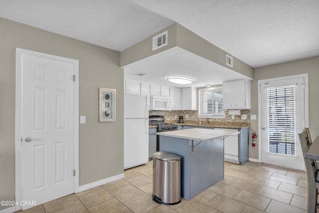 kitchen featuring white appliances, white cabinetry, backsplash, a center island, and a healthy amount of sunlight