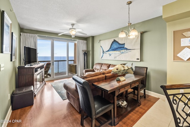 dining room featuring ceiling fan with notable chandelier, tile flooring, a textured ceiling, and a water view